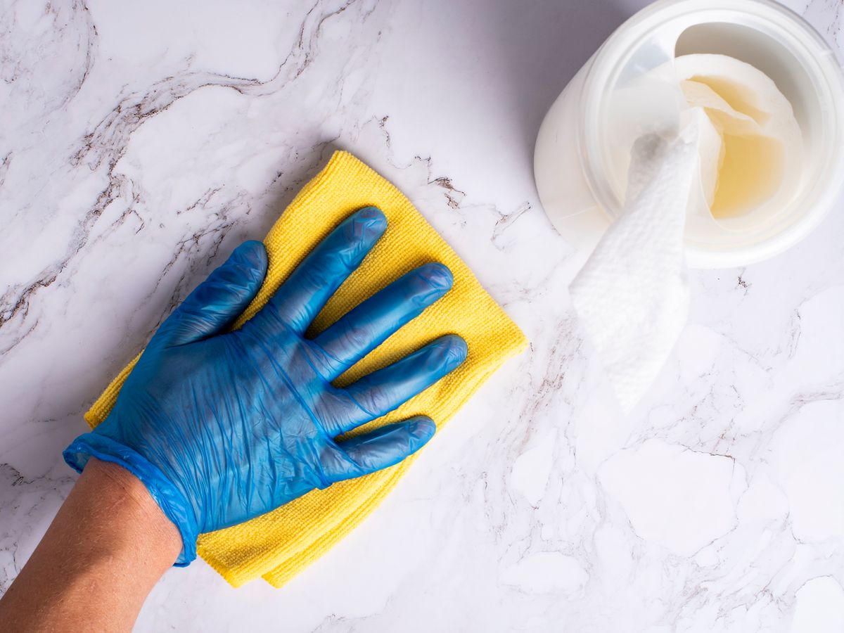 Mão com luva limpando superfície na cozinha